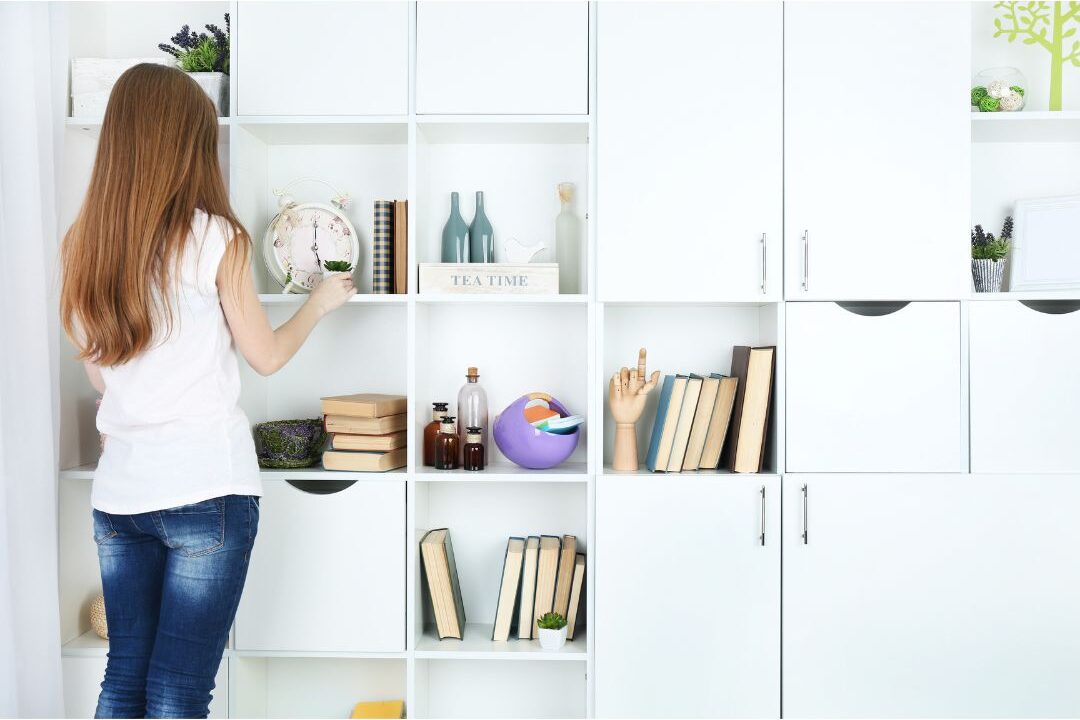 woman organizing living room surfaces and placing books on shelf fixing decor mistakes