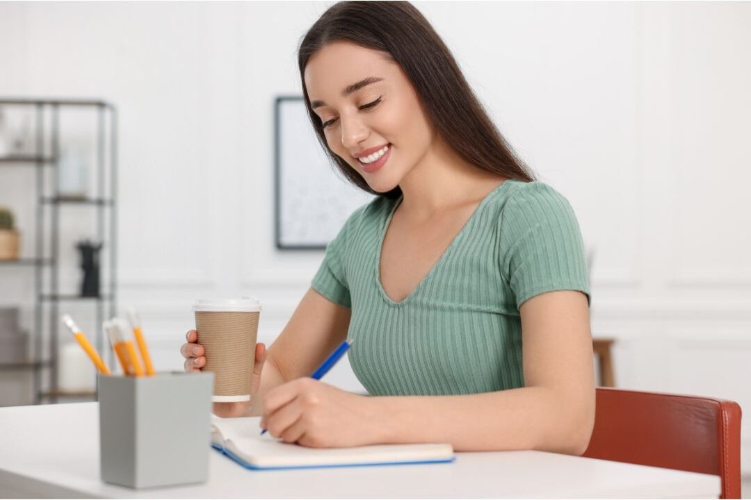 woman writing in a weekly planner with a cup of tea on her desk