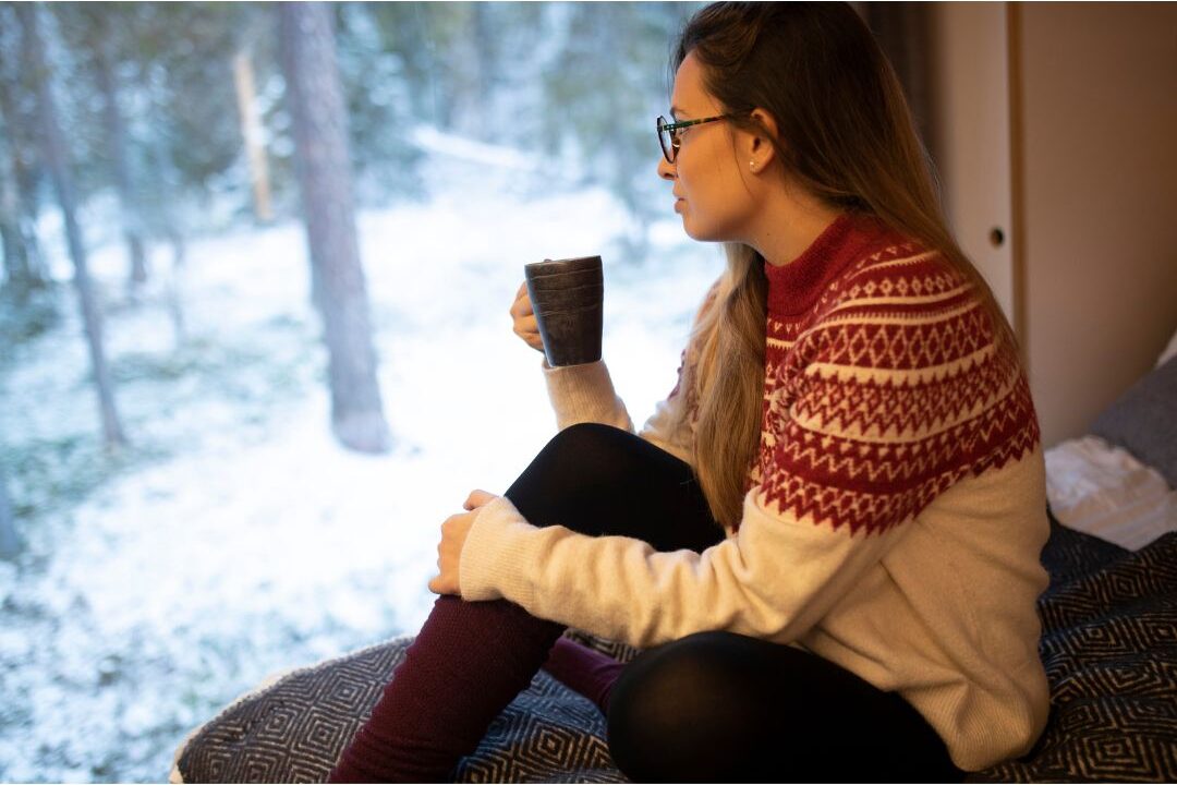 woman looking thoughtfully out a window while holding coffee planning for realistic business growth