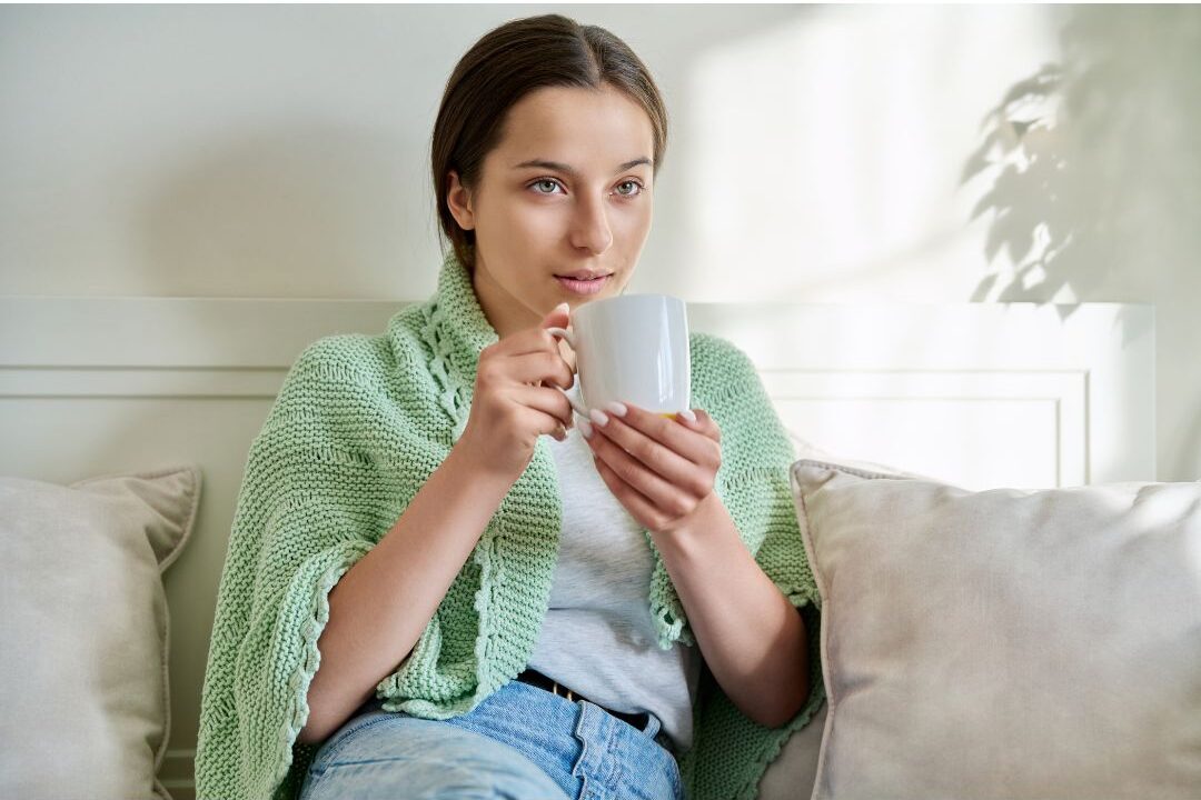 smiling mother sitting comfortably on couch holding a warm cup enjoying peaceful motherhood
