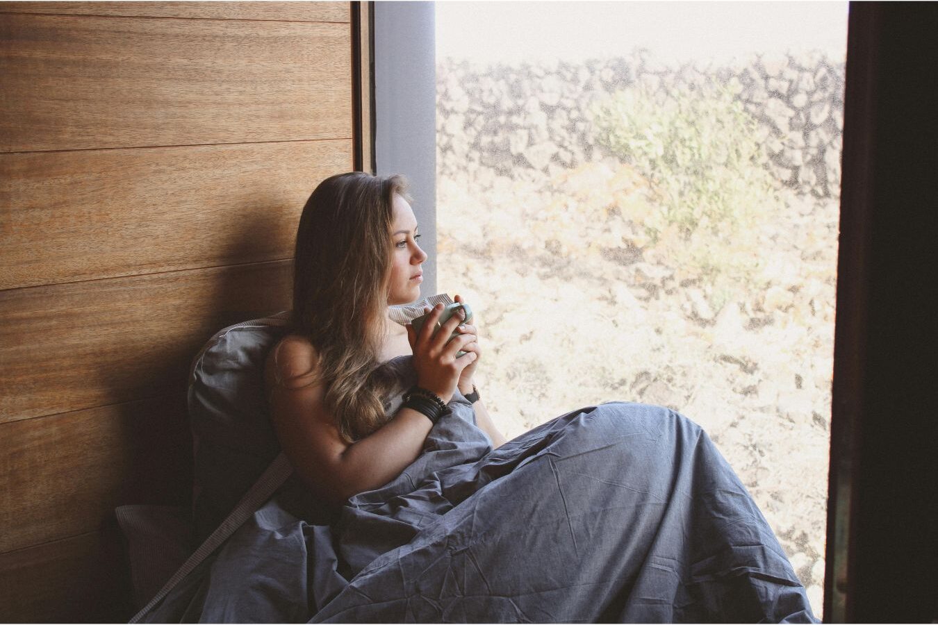 woman sitting comfortably on armchair holding warm cup near window enjoying morning peace