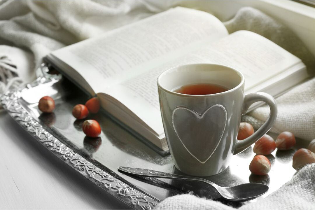 warm cup of herbal tea sitting on wooden tray next to an open book showing restful evening ritual