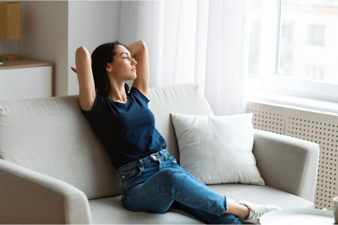 peaceful woman sitting on sofa enjoying clean organized home embracing home systems that practically run themselves