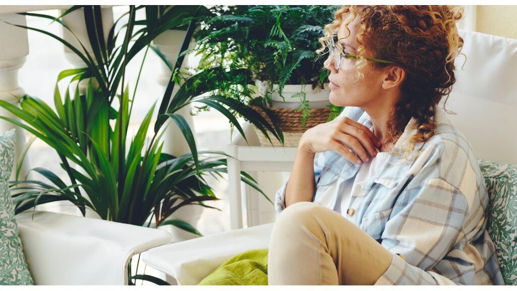 woman sitting peacefully outside on a sunny balcony with green plants enjoying mental rest