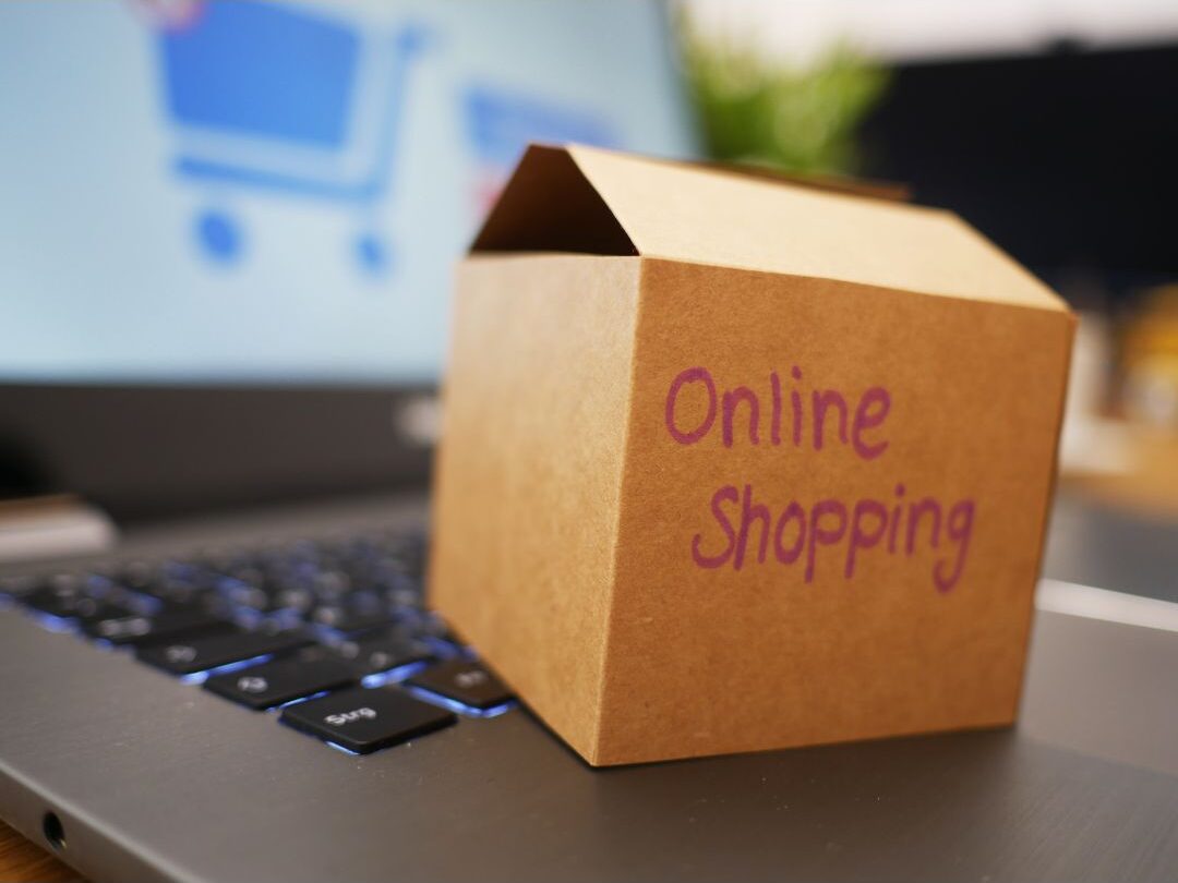 laptop displaying an online shopping cart next to delivery boxes showing hidden fees from the hidden expenses quietly destroying your budget