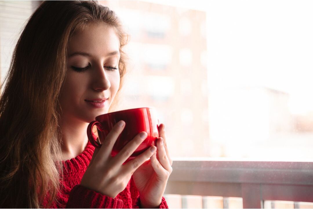 woman holding glass mug of tea near bright window demonstrating luxury habits anyone can afford