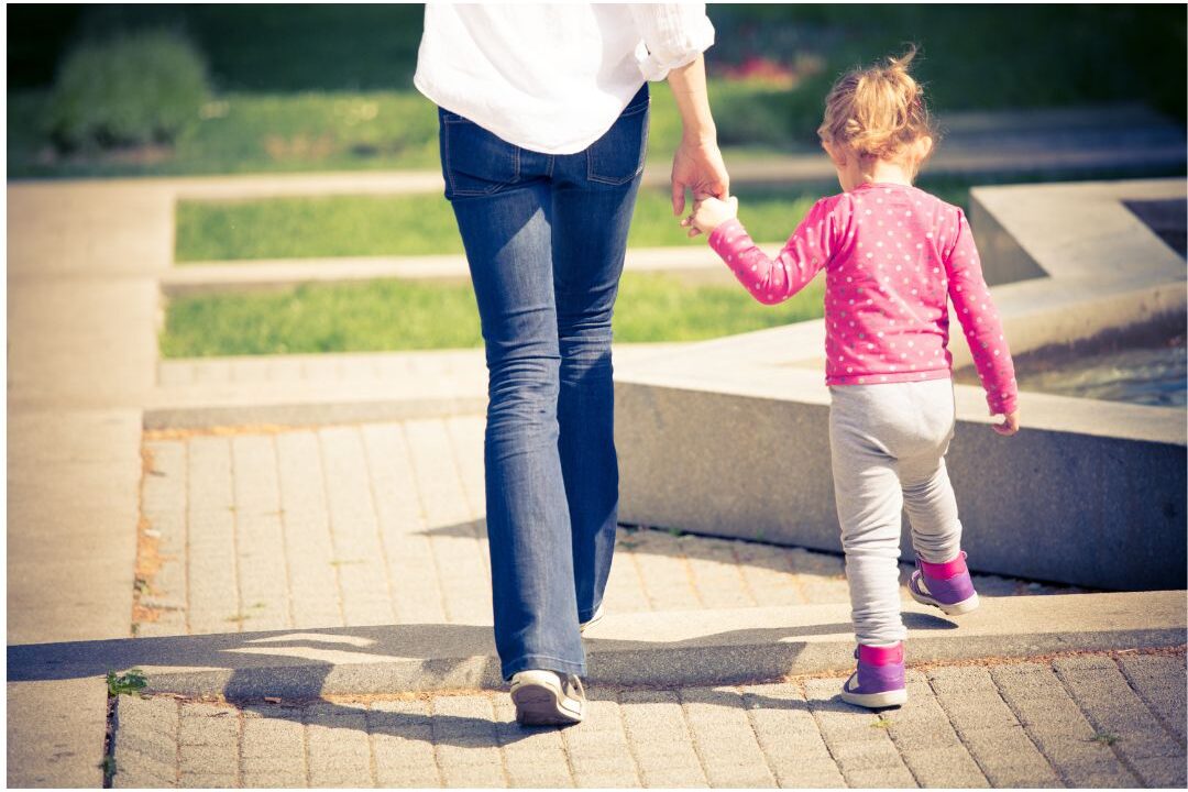 mother holding child's hand while walking down sunlit park trail demonstrating lasting impact