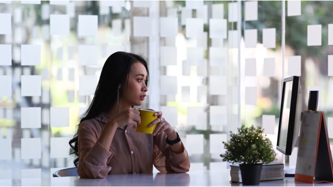 woman looking thoughtfully out a window holding a warm cup