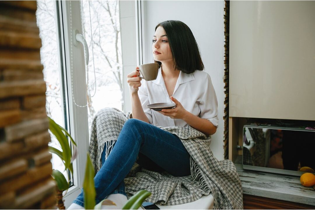 woman sitting near window holding warm mug looking relaxed embracing soft living