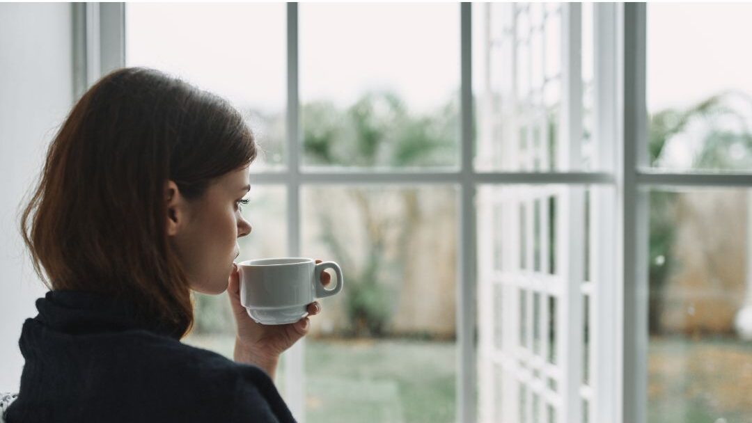 woman holding a warm mug near a sunny window looking serene learning how to stop feeling guilty about rest