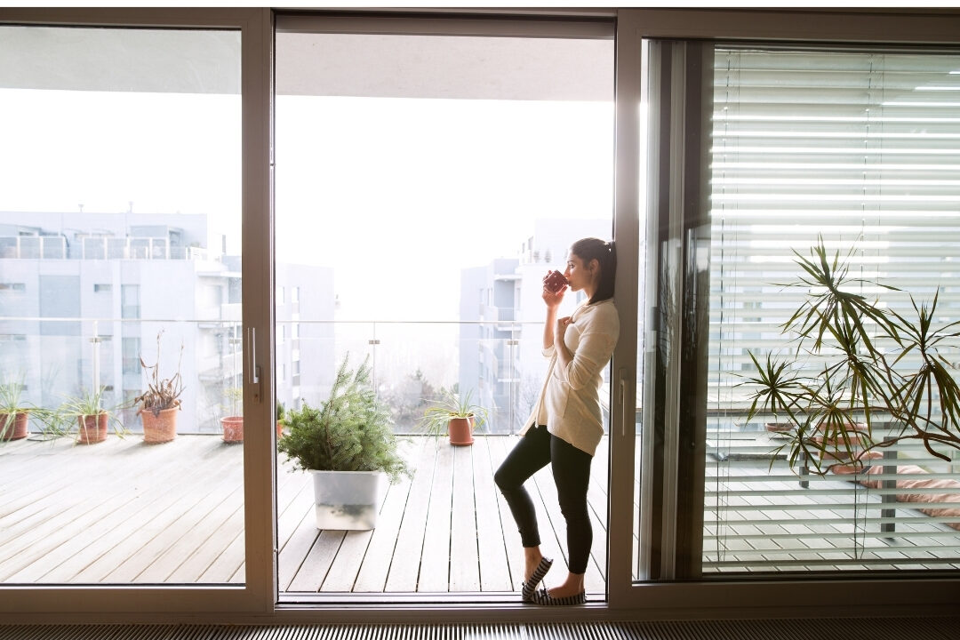 woman standing on sunny balcony drinking tea during work break taking intentional rest