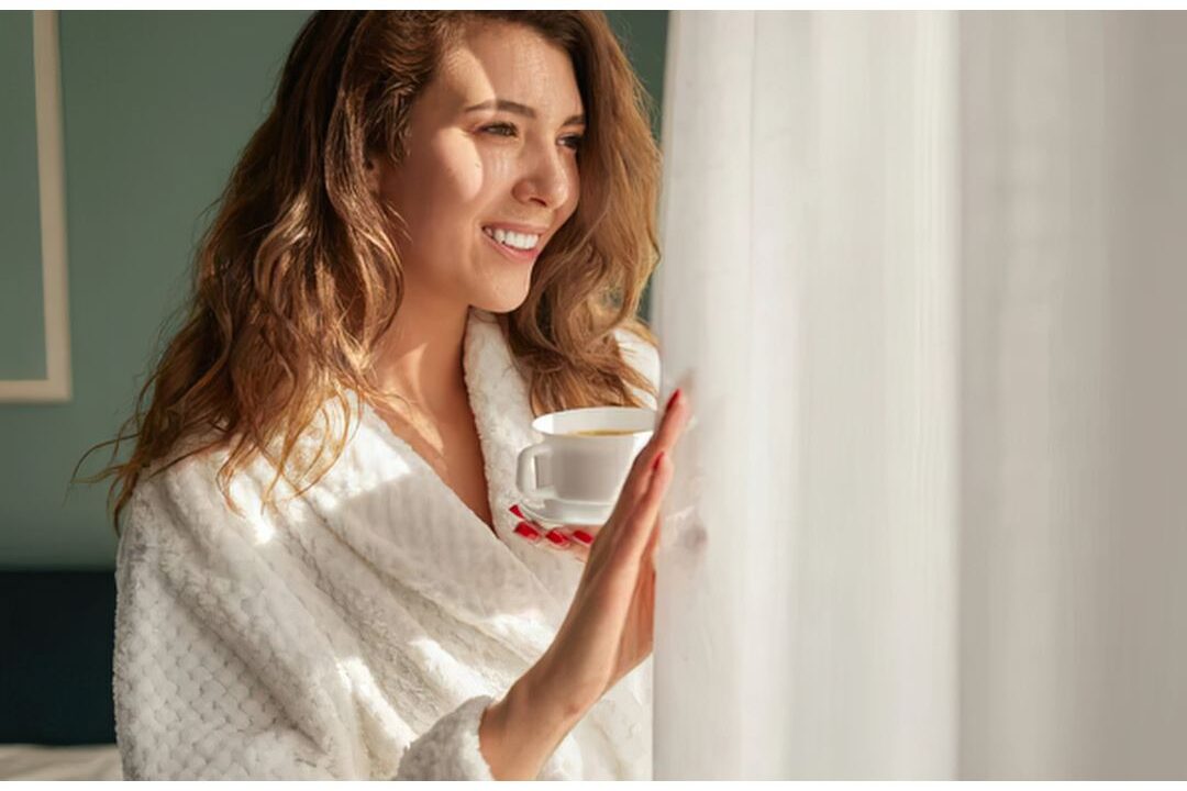 woman smiling peacefully looking out window holding warm cup celebrating the easiest digital products to sell this year