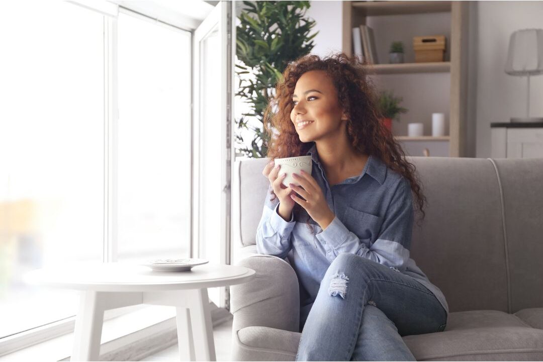 peaceful woman sitting by window drinking tea in cozy room avoiding time-wasting habits