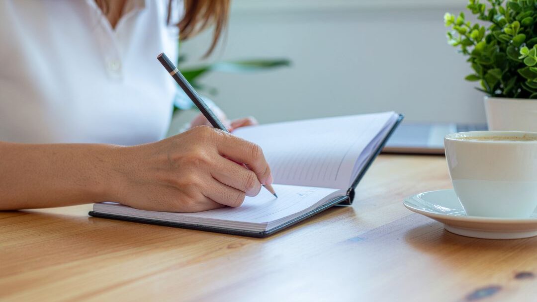 woman writing in notebook at warm sunlit desk with coffee understanding the hard truth about being home all day