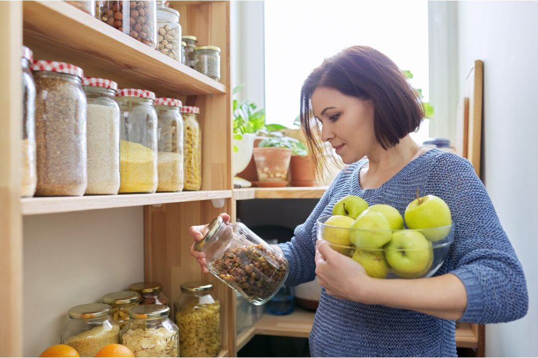 smiling woman organizing a clean kitchen shelf learning how to stop wasting money on these household items
