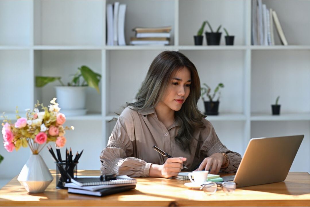 focused woman working on a laptop at a kitchen table reflecting on things I wish I knew before starting my first side hustle