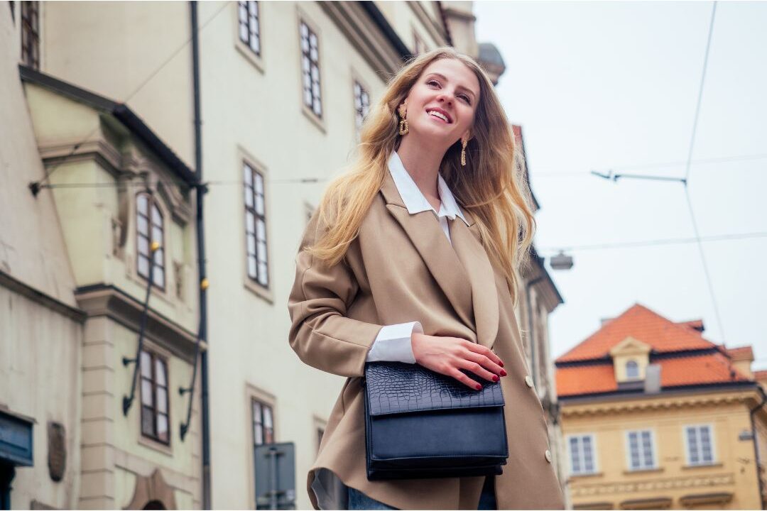 chic elegant woman in beige trench coat and leather bag walking on city street demonstrating things stylish women never buy