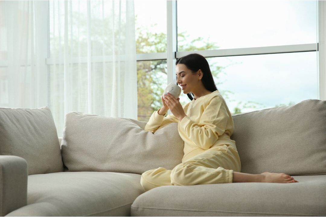 peaceful woman sitting on sofa drinking tea looking at clean living room avoiding wasting 3 hours every day