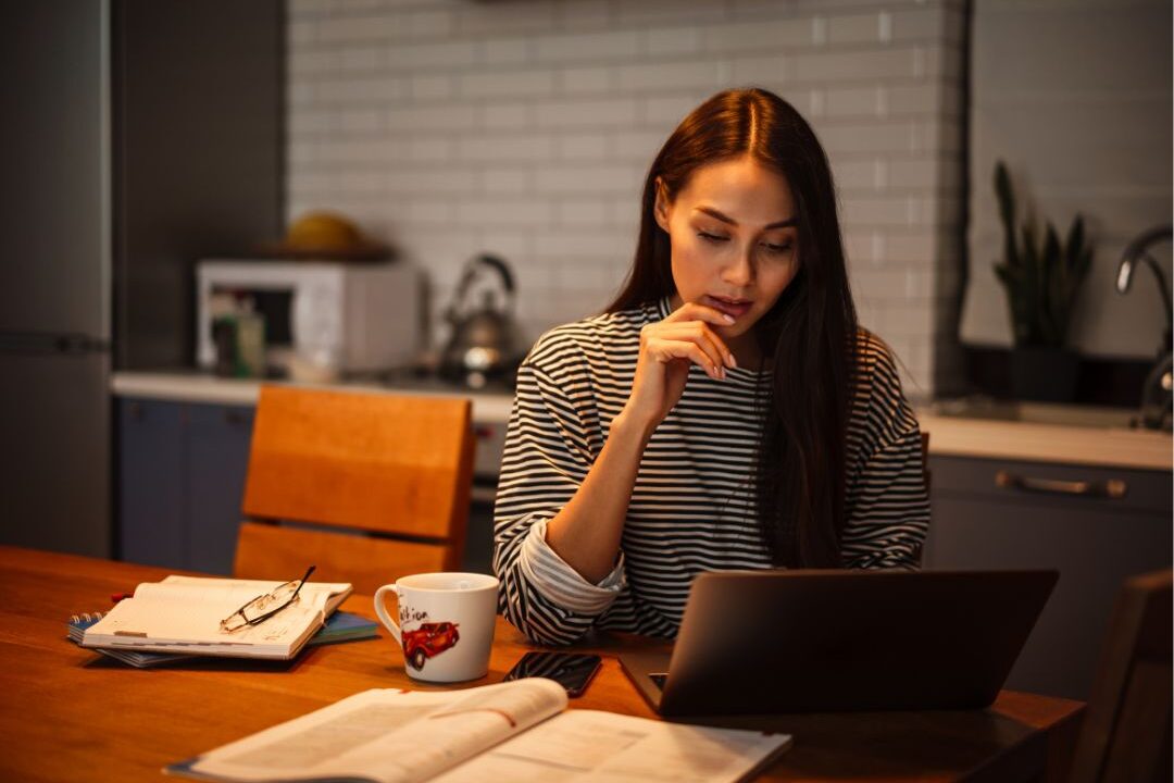 focused woman working on a laptop at a kitchen table learning why most moms never make money online