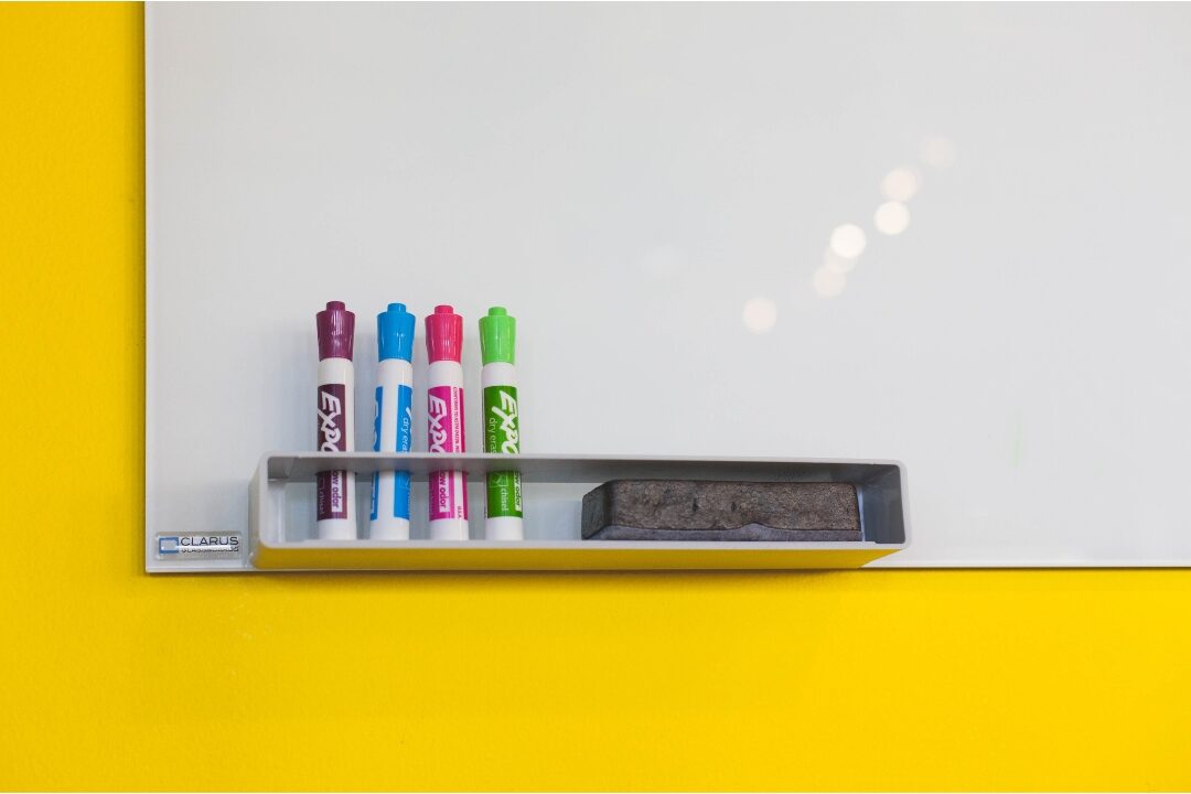 acrylic wall calendar with colorful dry erase markers on white wall tracking family schedules