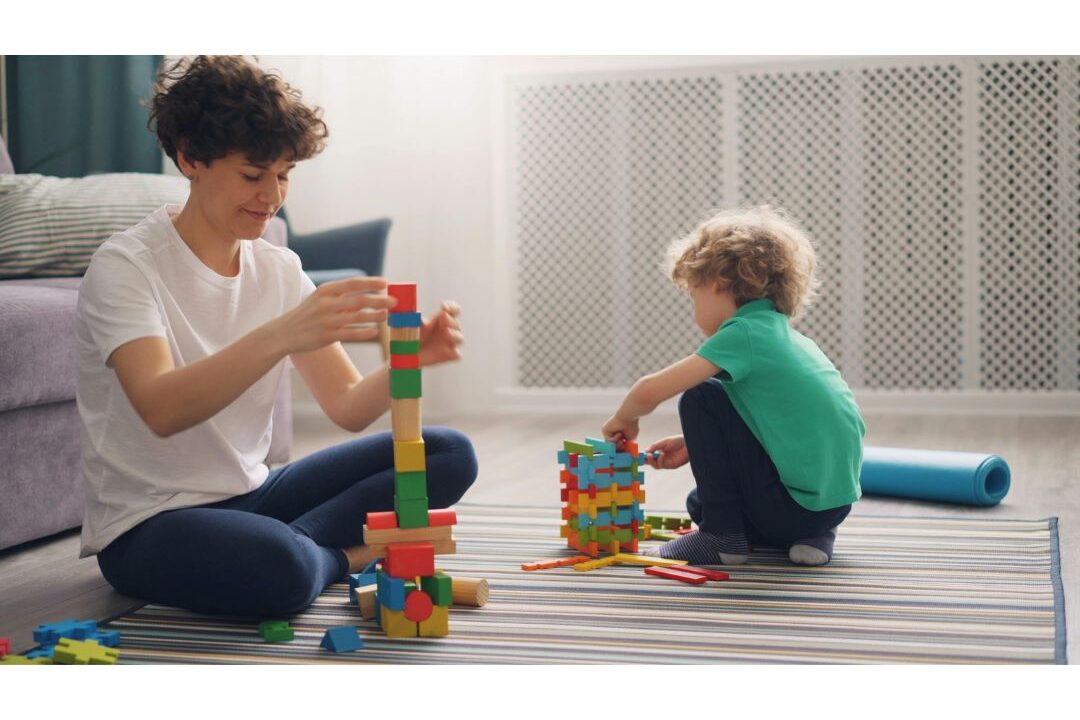 mom sitting on floor playing blocks attentively with child