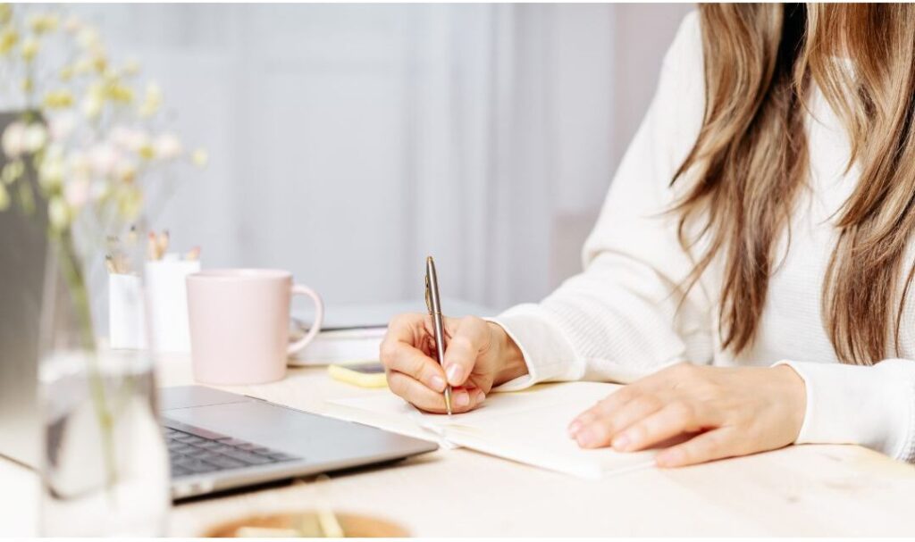 woman making notes in notebook auditing daily friction points showing the soft life checklist i wish every mom had before having kids