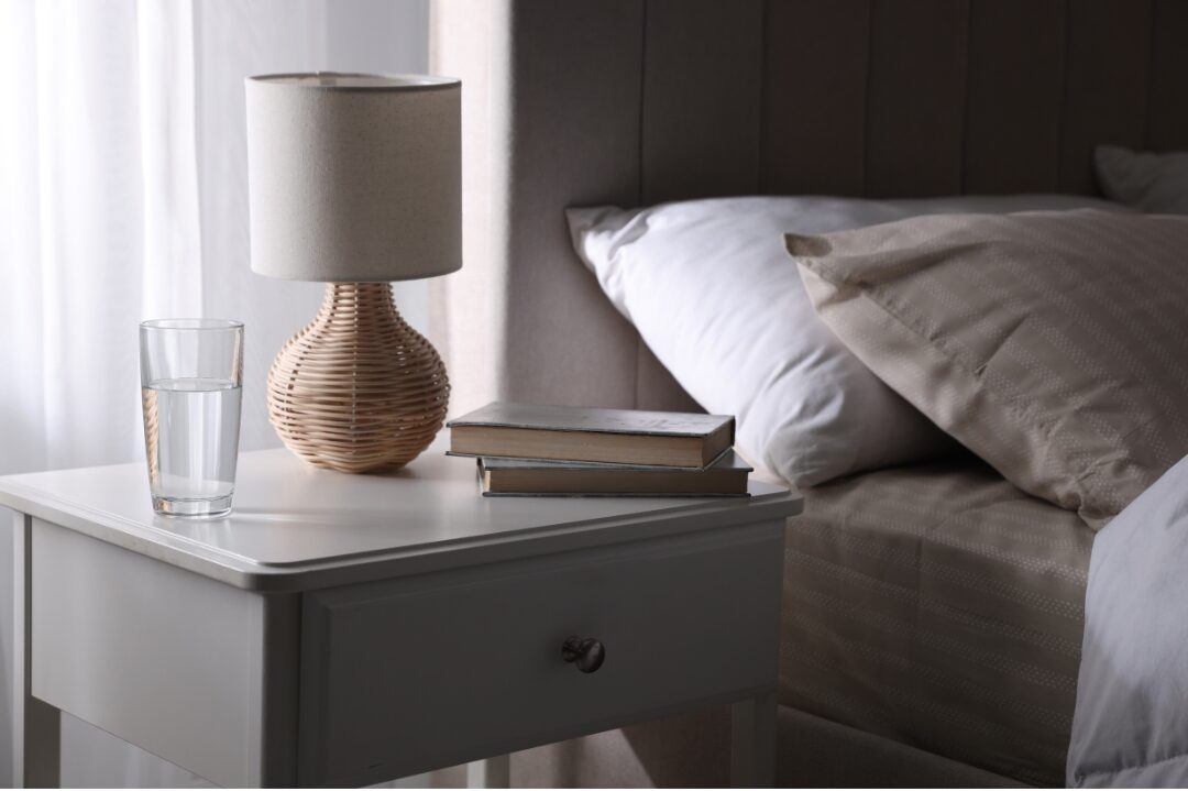 bedside nightstand with a clean glass water carafe and simple lamp