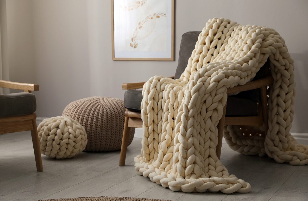 chunky knit beige throw blanket draped casually over textured bouclé armchair displaying 40 cozy home ideas you'll want to copy