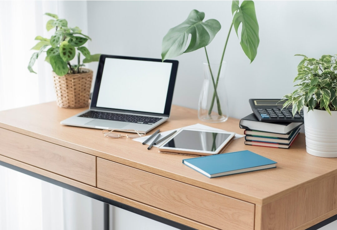 clean wooden home office desk with a laptop and small notebook reviewing 101 things to declutter this weekend