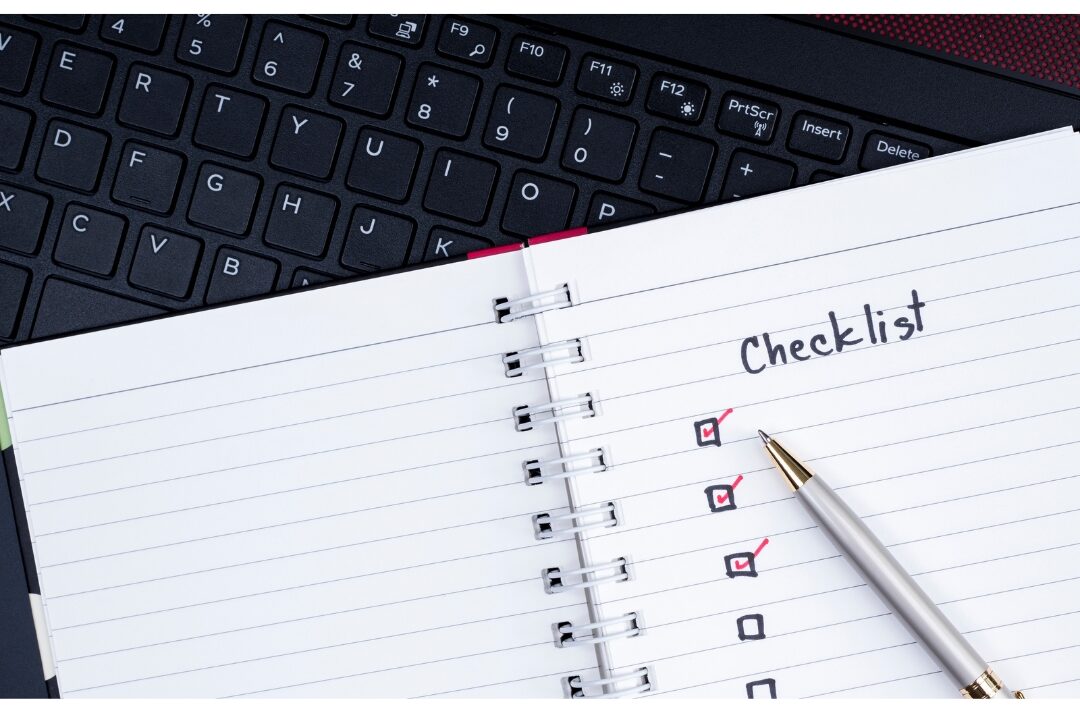 paper notepad with handwritten shutdown checklist beside laptop organizing daily tasks