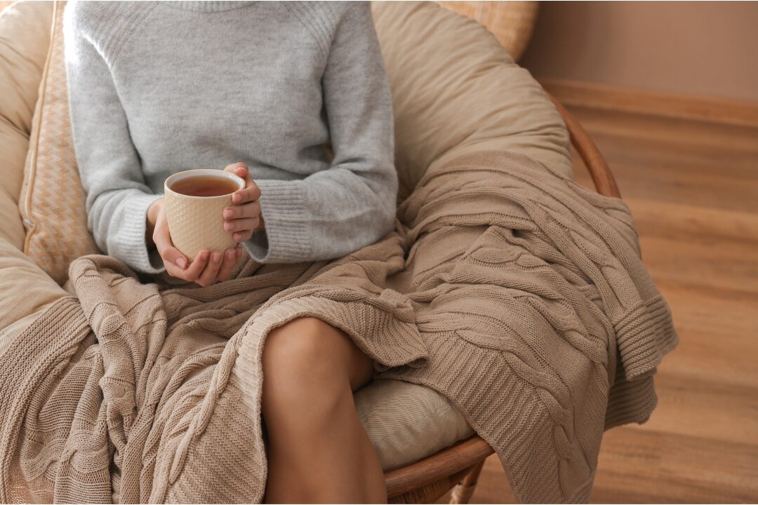 woman resting comfortably with a warm cup of tea in cozy chair practicing self-compassion