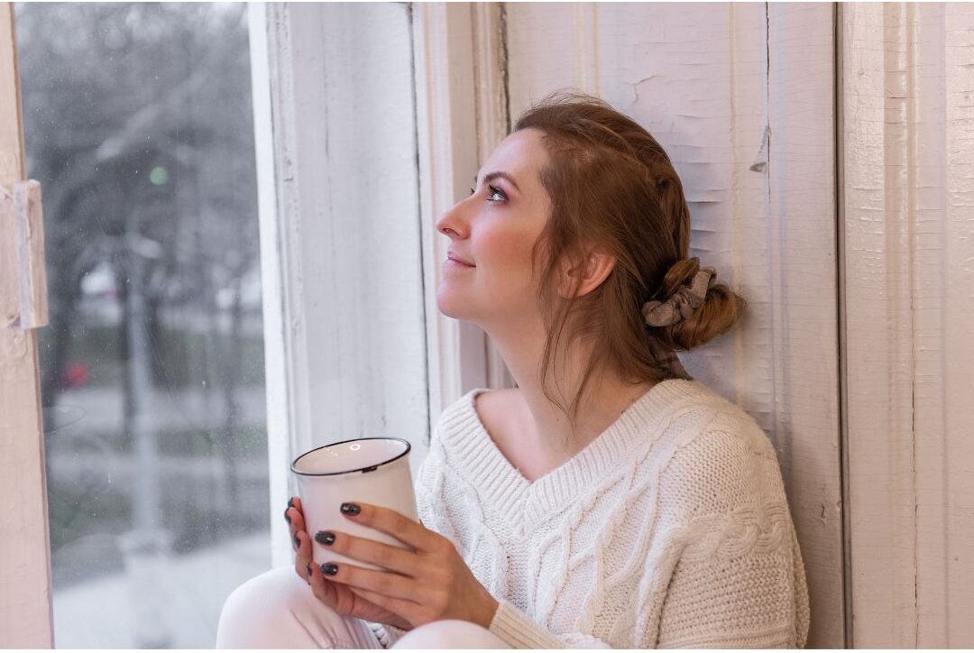 peaceful mom drinking warm tea sitting on sunny kitchen window bench illustrating 45 daily habits that make life easier