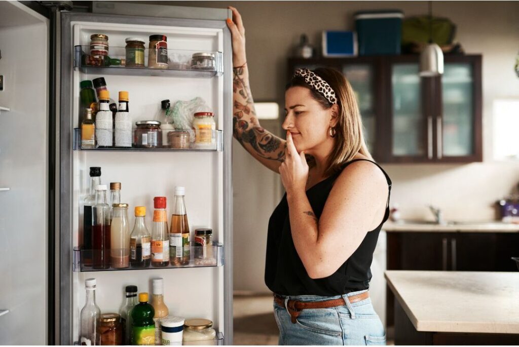 stressed mother looking into open kitchen refrigerator deciding dinner
