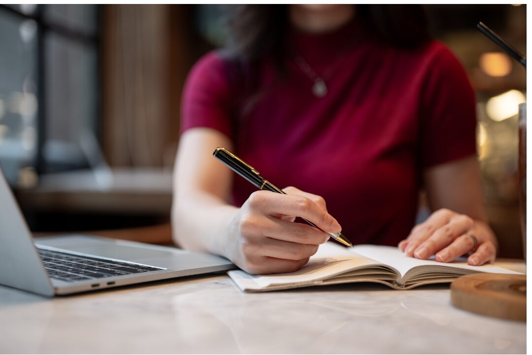 woman sitting at desk looking at notebook with pen in hand overcoming afternoon paralysis