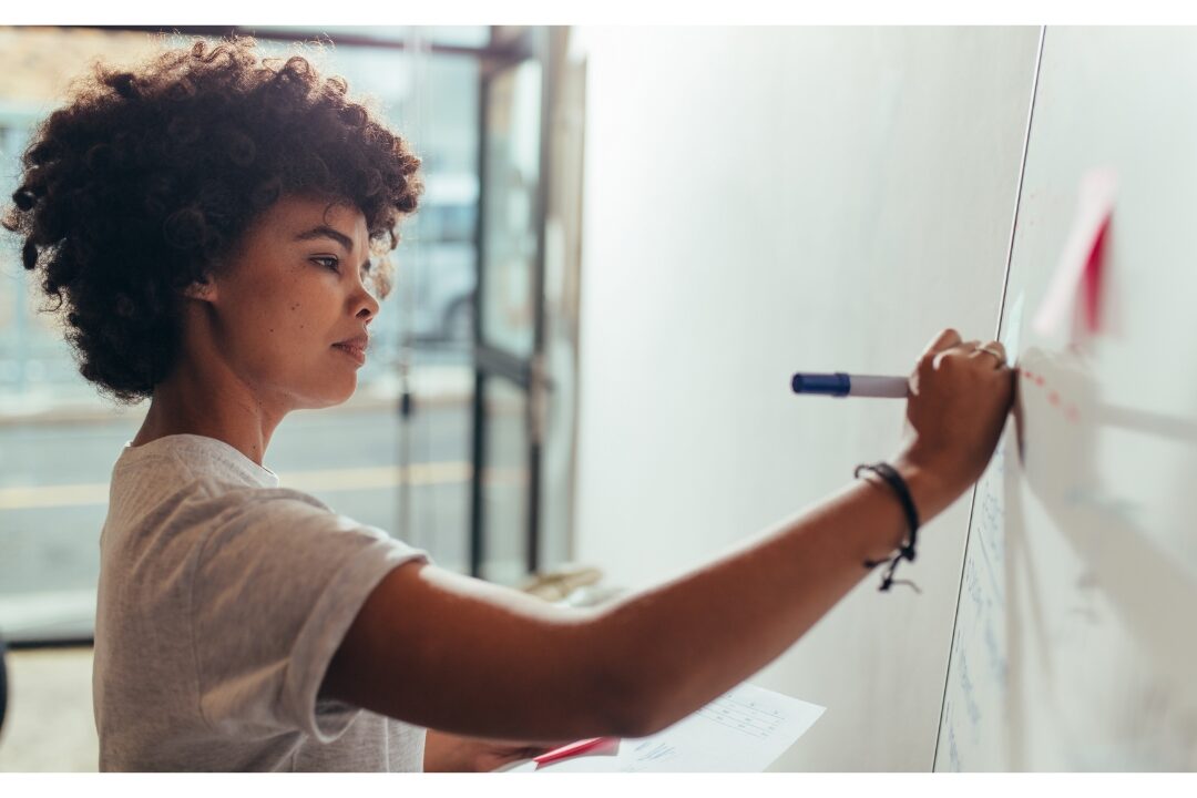 woman updating white dry erase calendar with marker during Sunday reset maintaining the family command center every busy home needs