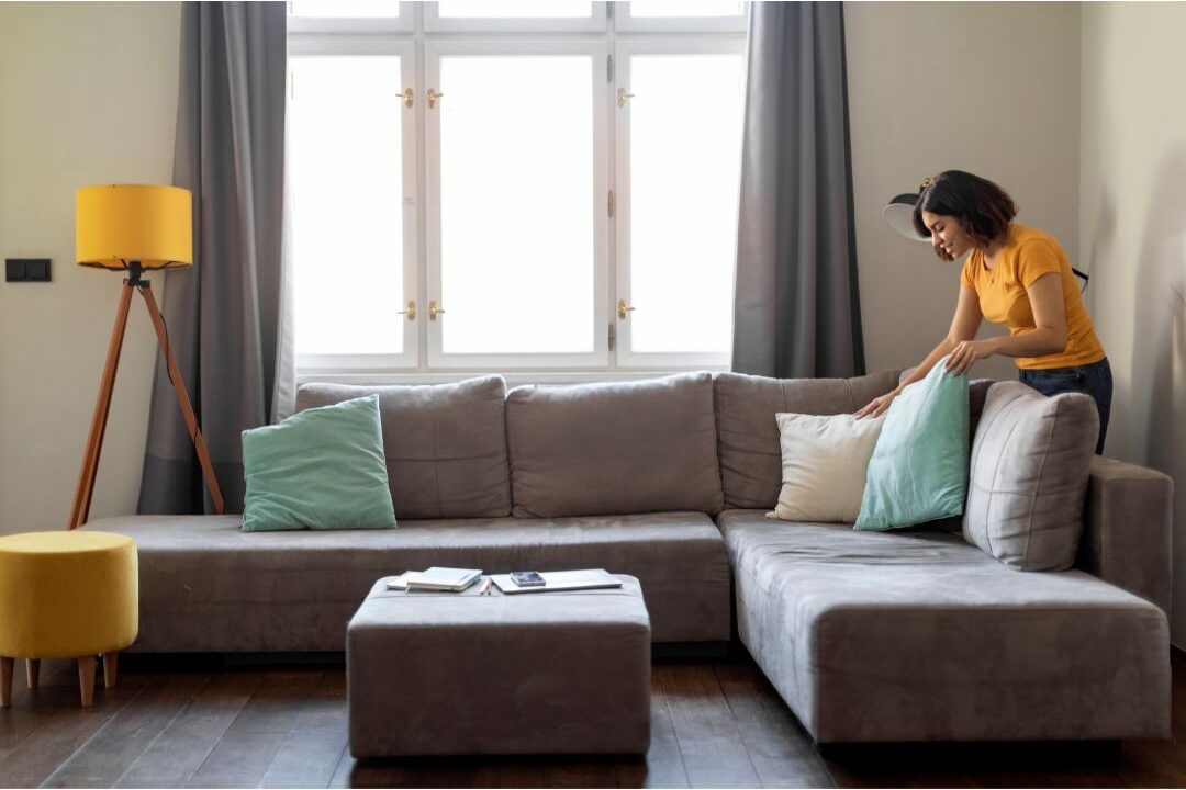 woman fluffing sofa cushions in warm tidy living room