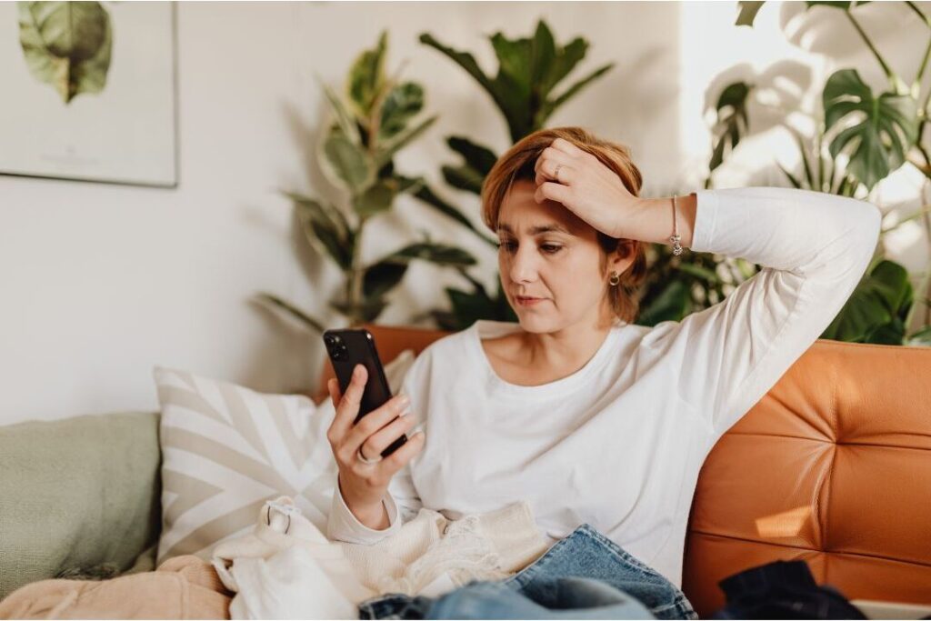 exhausted mother holding phone illustrating emotional spending habits that keep families broke