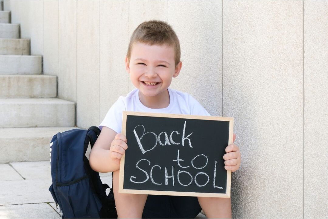 happy child posing with back to school chalkboard sign outside sunny front door highlighting 25 family traditions worth starting
