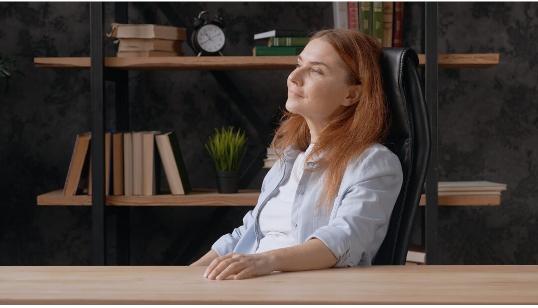 woman sitting peacefully at sunlit desk looking relaxed presenting 30 tiny luxuries every woman deserves