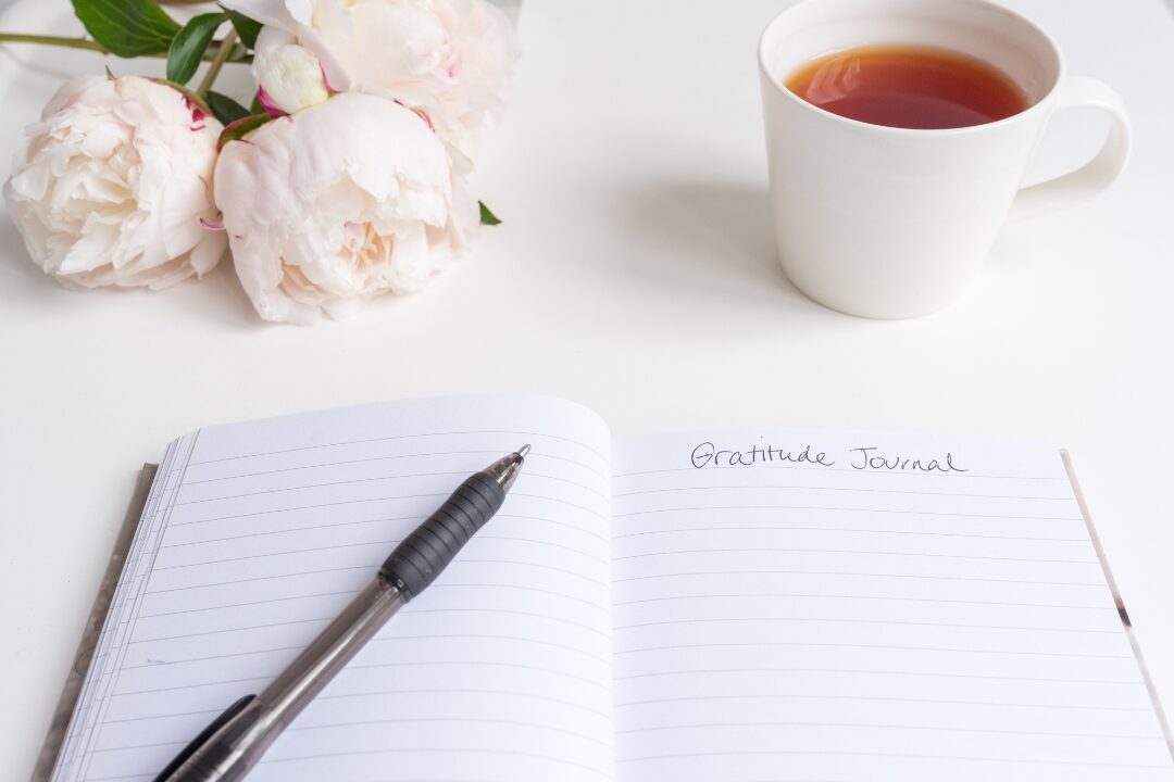 open journal displaying handwritten gratitude notes beside warm tea cup practicing daily gratitude