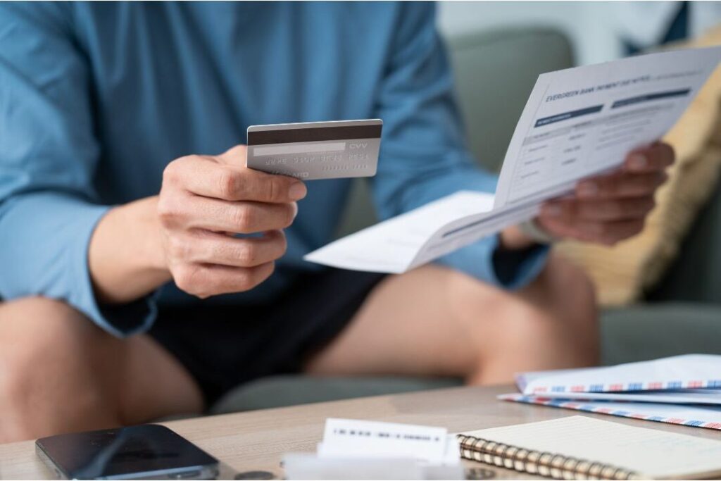person holding credit card over paper bills showing debt habits that keep families broke