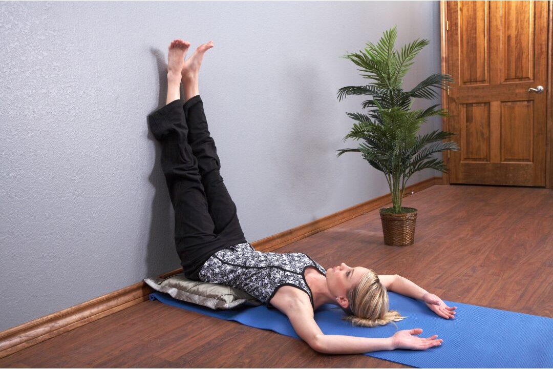 woman resting comfortably on yoga mat with legs resting up wall