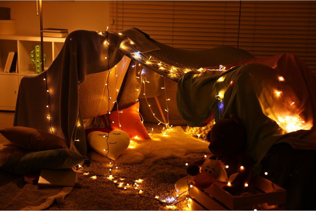 living room blanket fort with fairy lights and sleeping bags inside at night