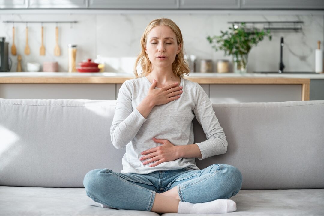woman taking a deep calm breath with eyes closed at office desk releasing work stress