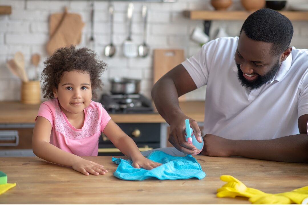 father and young child wiping kitchen table together happily highlighting things mentally strong moms do differently