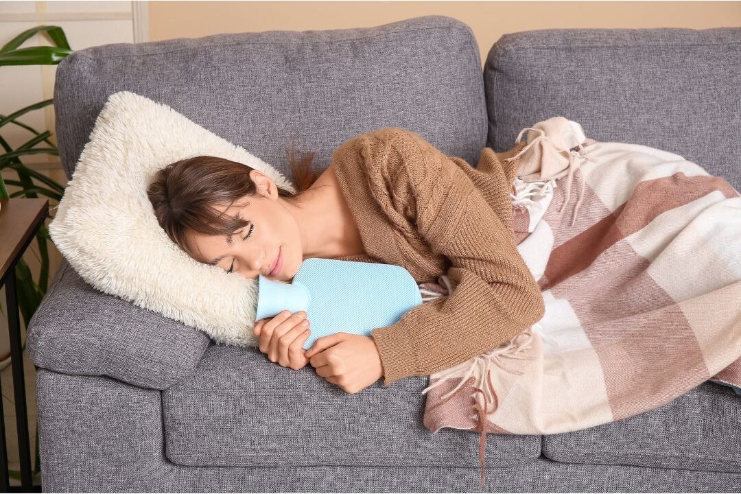woman resting under warm throw blanket with hot water bottle