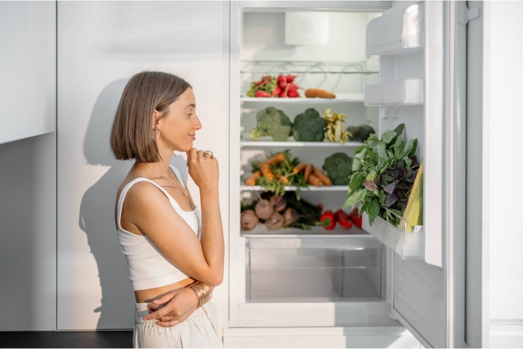 woman looking at open refrigerator with thoughtful expression experiencing decision fatigue