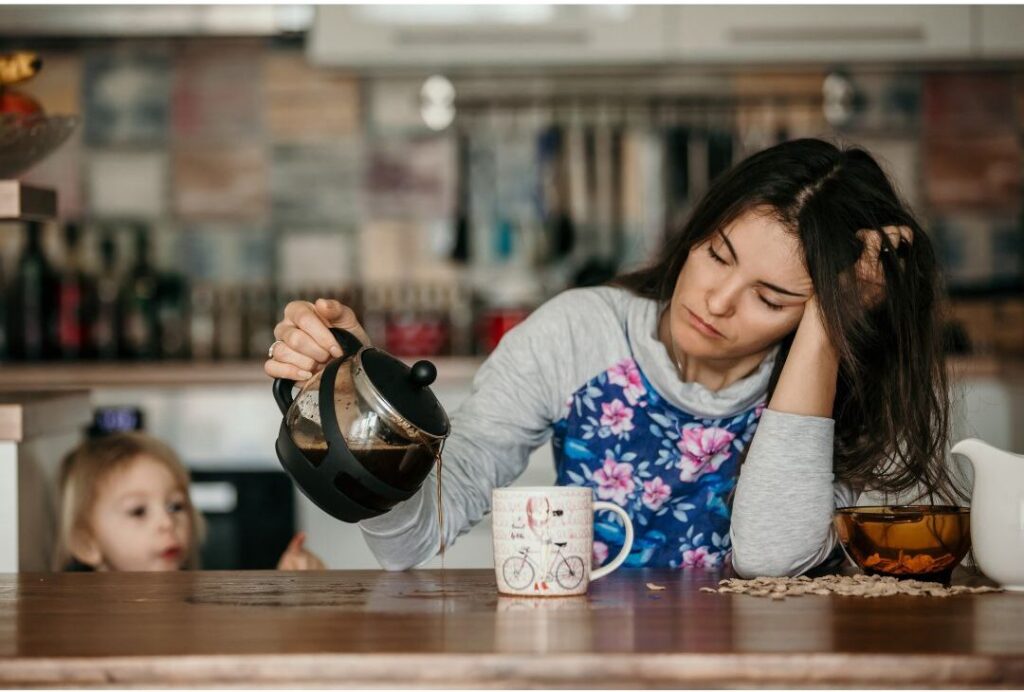 exhausted mother sitting quietly at sunlit wooden kitchen table exploring why nobody talks about this reason moms feel exhausted