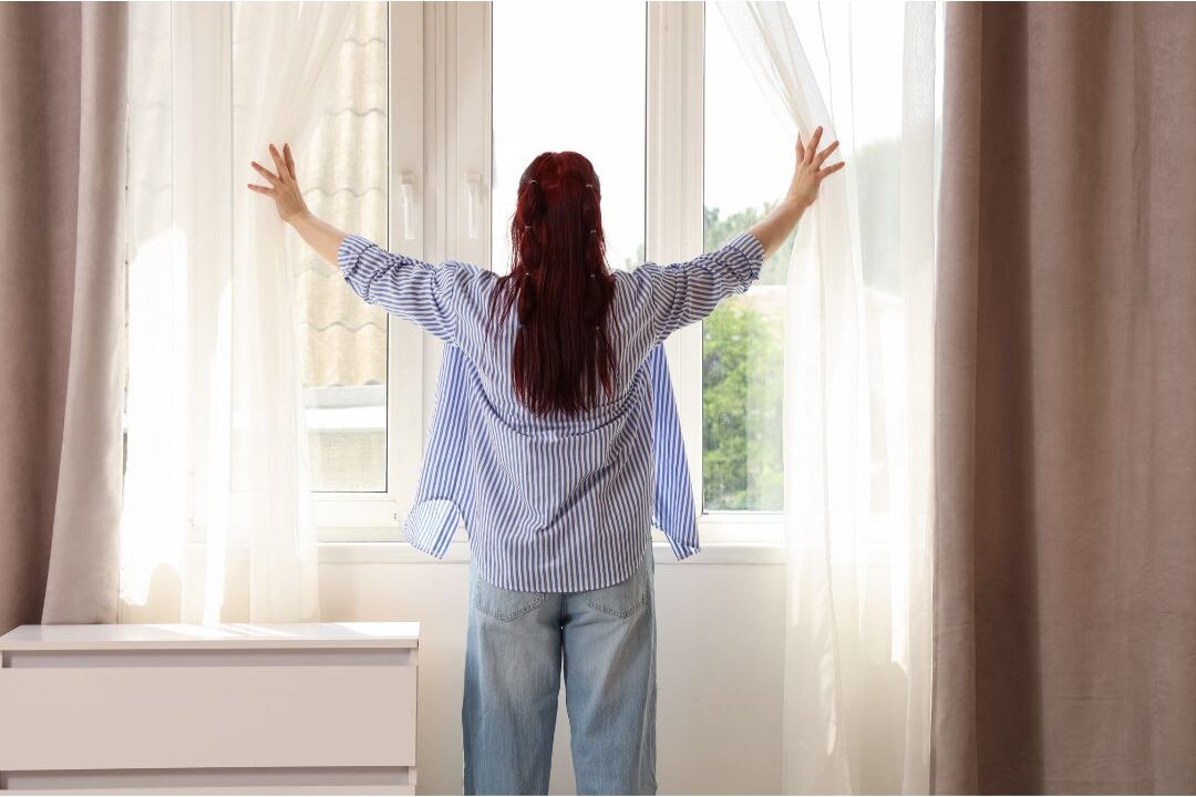 hands opening white sheer curtains to let bright morning sun inside