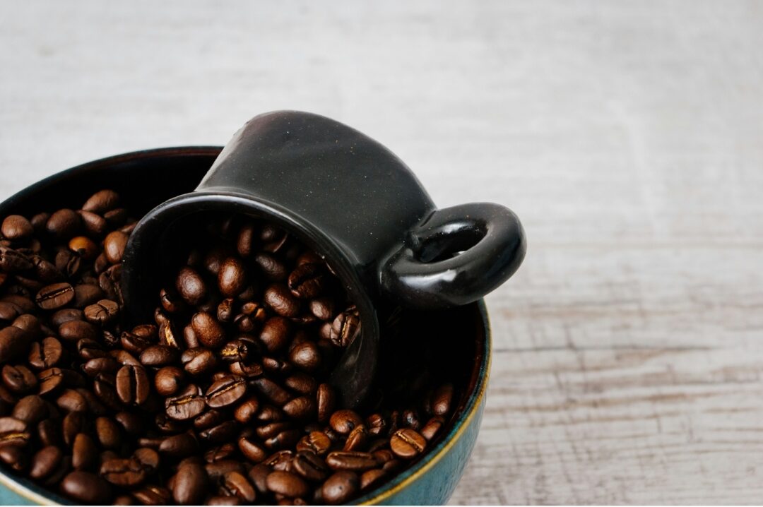 freshly roasted brown coffee beans overflowing in small ceramic bowl